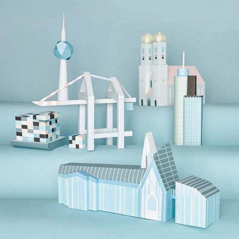 Bunte, stilisierte Architekturmodelle aus Papier auf blassem Hintergrund angeordnet.