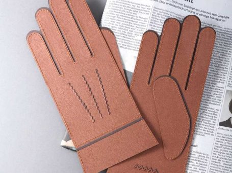 Braune Papierhandschuhe aus Papier und genäht auf einer Zeitungsseite.