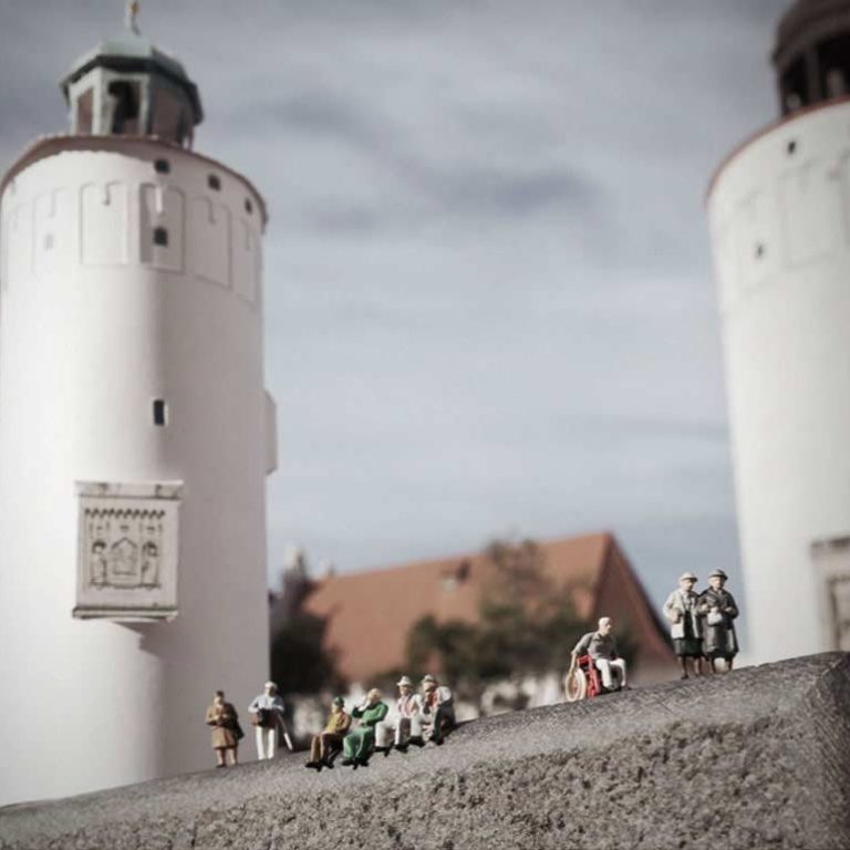 Miniaturisierte Figuren vor Frauenturm in Görlitz aus Papier, umgeben von einer Landschaft.