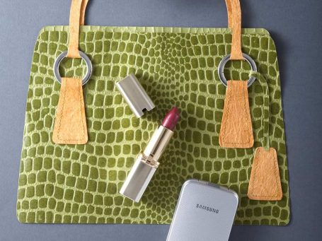 Grüne Handtasche aus Papier mit ledernen Trägern, Lippenstift und einem kleinen Makeup-Spiegel.